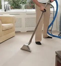 Professional carpet cleaner using a hot-water extraction wand and hose machine in a living room in Stamford, CT.