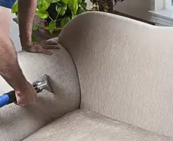 Professional upholstery cleaner deep-cleaning a fabric sofa with a handheld extraction tool and hose in Stamford, CT.